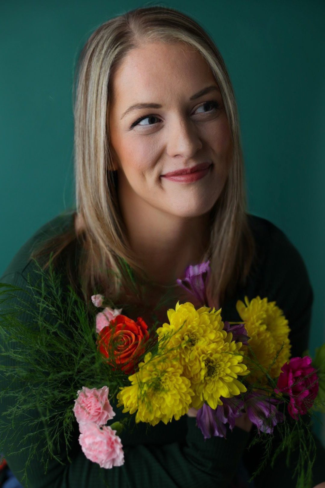 Portrait of Ashley, a professional photographer, gazing thoughtfully to the side, with a bouquet of vibrant flowers.