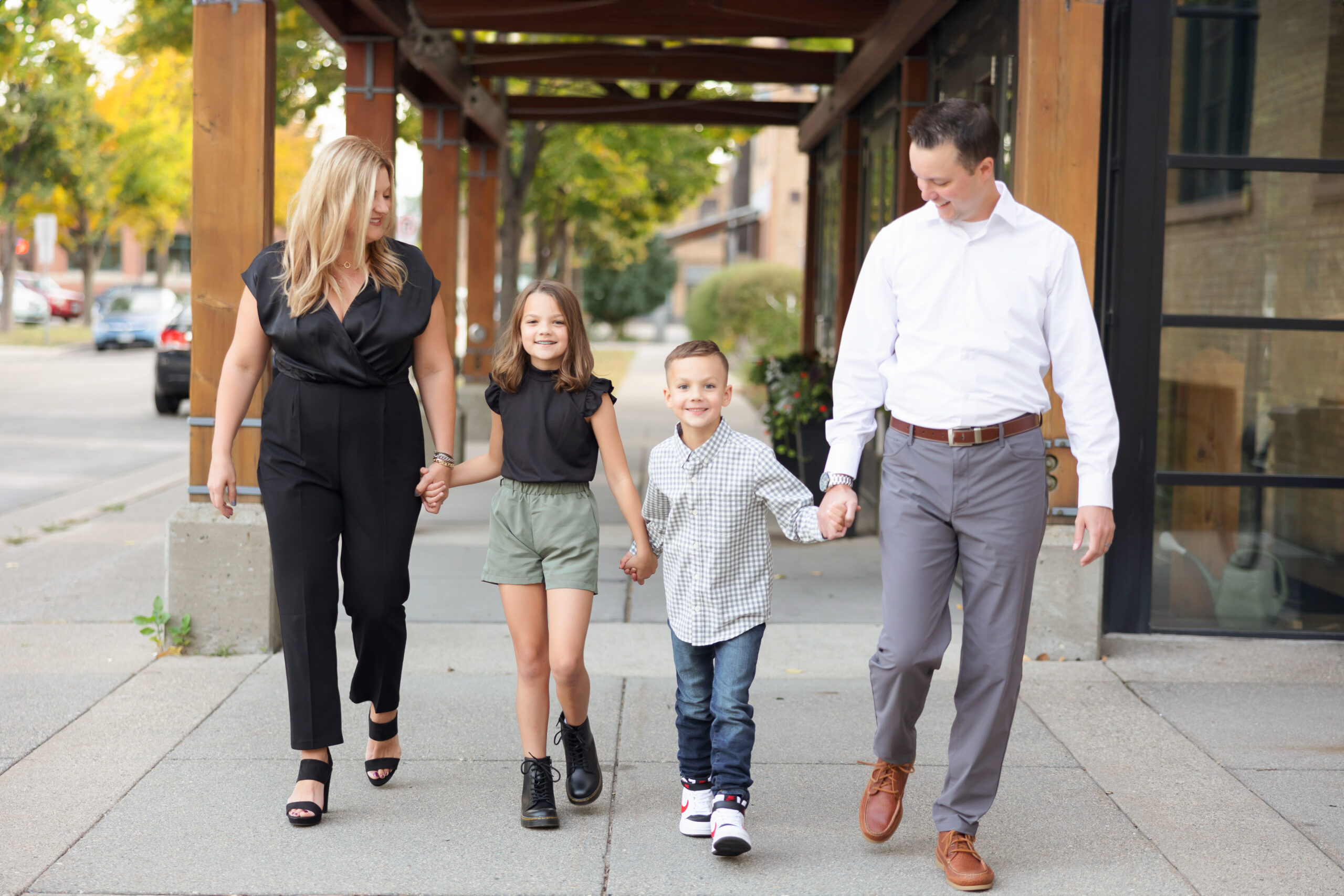 A family of four strolling hand-in-hand along a city sidewalk, exuding stylish urban charm.